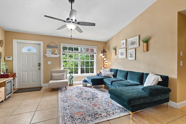 living area featuring light tile patterned floors, a textured ceiling, a ceiling fan, and baseboards