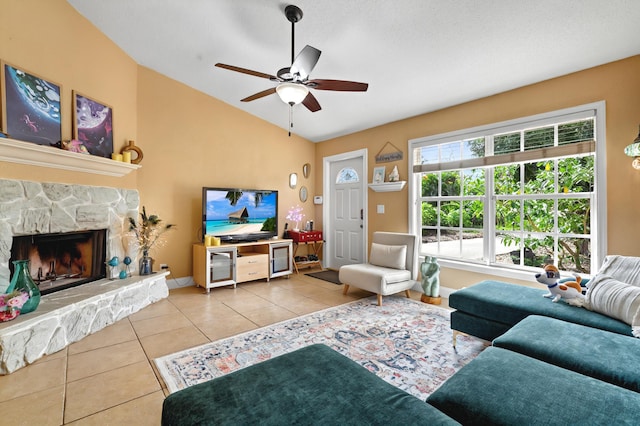 living room featuring lofted ceiling, ceiling fan, a stone fireplace, tile patterned flooring, and baseboards