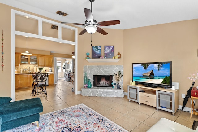 living room featuring a stone fireplace, light tile patterned flooring, visible vents, and a ceiling fan