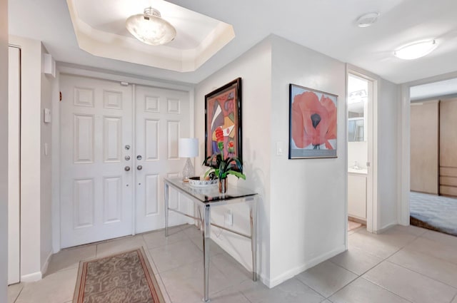 foyer entrance with a tray ceiling, baseboards, and light tile patterned floors