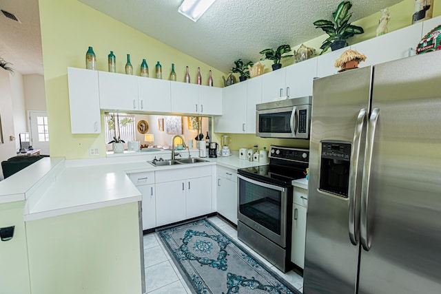 kitchen with appliances with stainless steel finishes, vaulted ceiling, a textured ceiling, a sink, and light tile patterned flooring