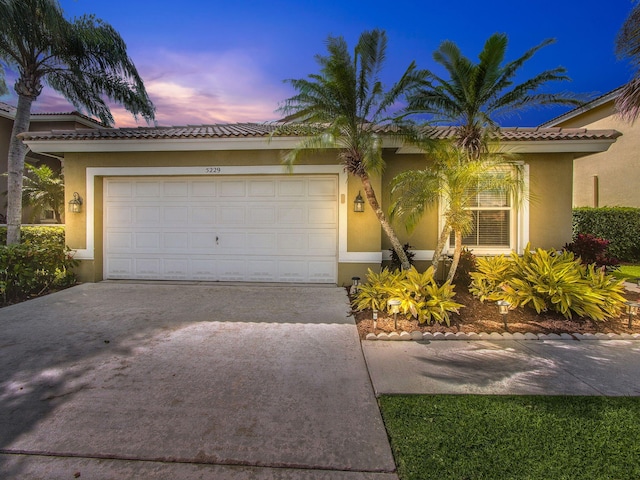 view of front of property featuring a garage, driveway, a tiled roof, and stucco siding