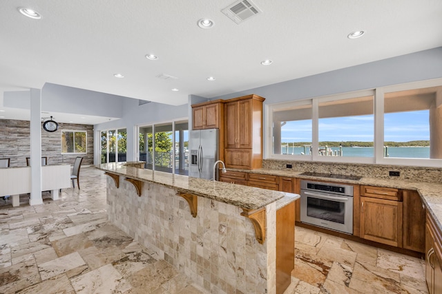 kitchen with light stone counters, brown cabinets, stainless steel appliances, visible vents, and a kitchen breakfast bar