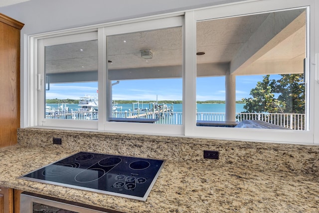 kitchen with light stone counters, a wealth of natural light, a water view, and black electric stovetop