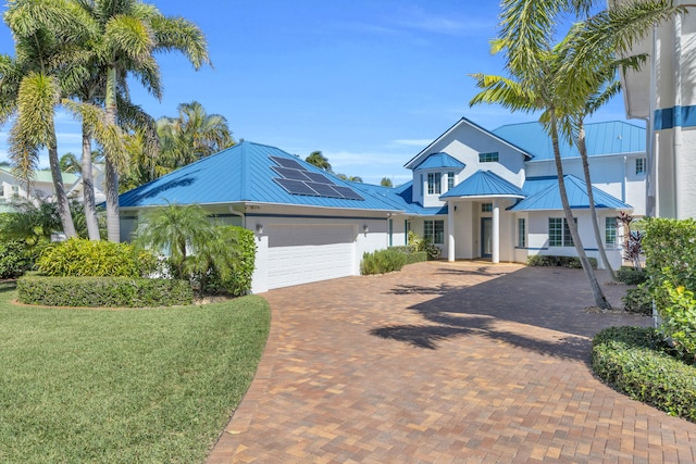 view of front of house with decorative driveway, an attached garage, a standing seam roof, metal roof, and a front lawn