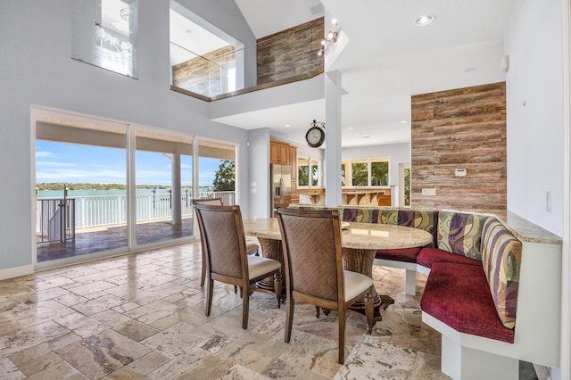 dining space with recessed lighting, stone tile flooring, a water view, a high ceiling, and baseboards