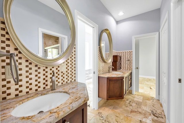 bathroom featuring tasteful backsplash, stone tile flooring, two vanities, and a sink