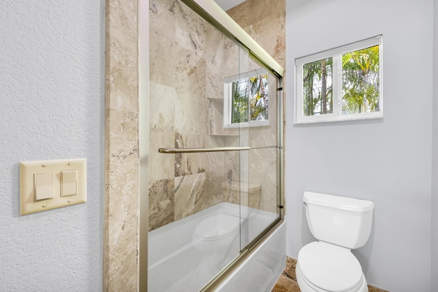 bathroom with bath / shower combo with glass door and toilet