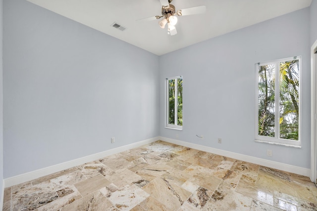 empty room with stone finish floor, baseboards, visible vents, and a ceiling fan