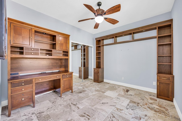 unfurnished office featuring stone finish flooring, ceiling fan, and baseboards