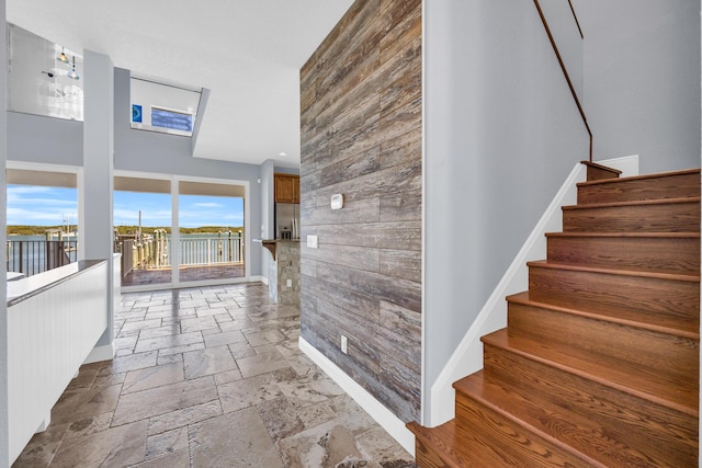 corridor featuring stone tile floors, a high ceiling, wood walls, baseboards, and stairs