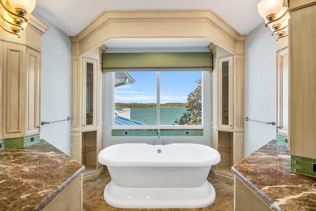 bathroom with backsplash, a water view, a freestanding tub, and decorative columns