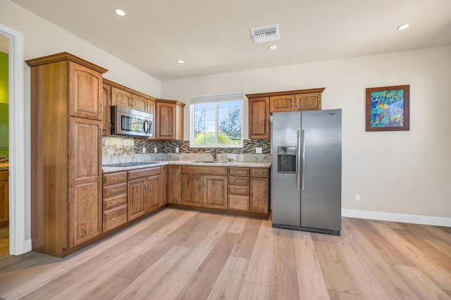 kitchen featuring stainless steel appliances, a sink, visible vents, decorative backsplash, and brown cabinetry