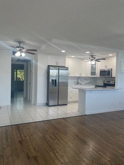 kitchen featuring light wood-type flooring, light countertops, appliances with stainless steel finishes, a peninsula, and white cabinetry