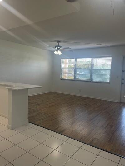 empty room with a ceiling fan, light wood-type flooring, and baseboards