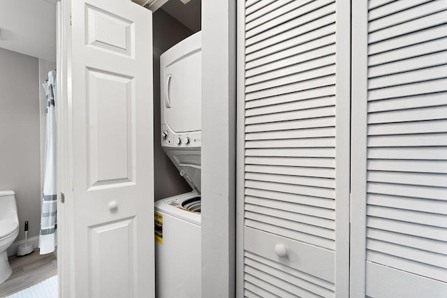 clothes washing area featuring stacked washer and dryer, laundry area, and wood finished floors