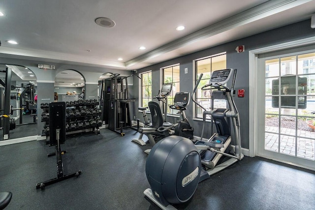 workout area featuring baseboards, a raised ceiling, arched walkways, ornamental molding, and recessed lighting