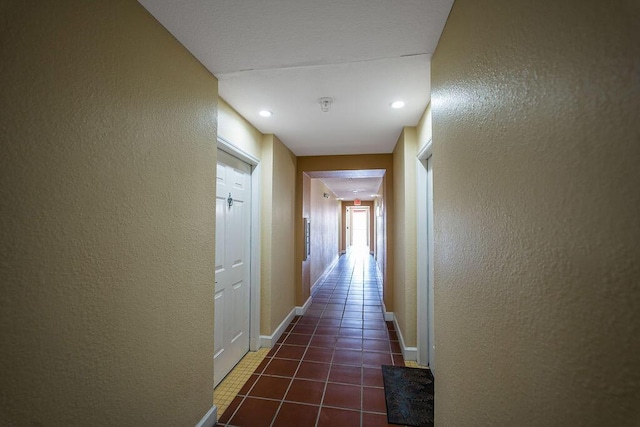 hall featuring a textured wall, dark tile patterned floors, and baseboards