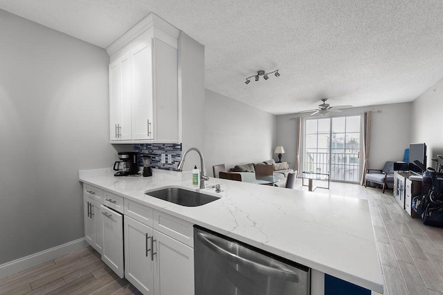 kitchen featuring tasteful backsplash, stainless steel dishwasher, open floor plan, a sink, and light wood-type flooring