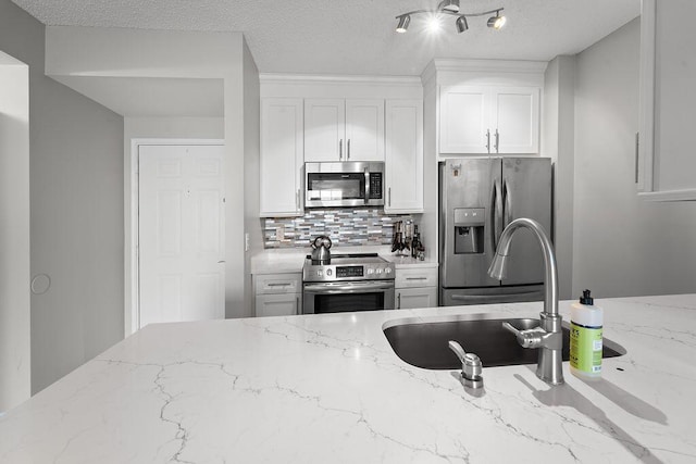 kitchen with white cabinets, a sink, light stone countertops, stainless steel appliances, and backsplash