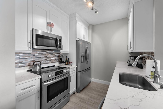 kitchen with decorative backsplash, appliances with stainless steel finishes, a textured ceiling, white cabinetry, and a sink