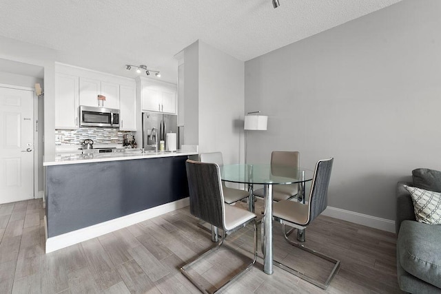 dining room featuring a textured ceiling, wood finished floors, and baseboards