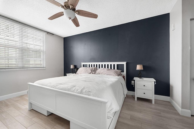 bedroom featuring light wood-style floors, an accent wall, baseboards, and a textured ceiling