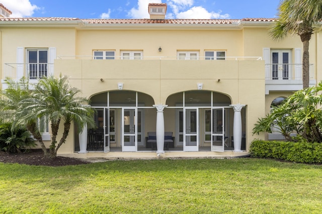 back of property featuring a sunroom, a tile roof, a lawn, and stucco siding