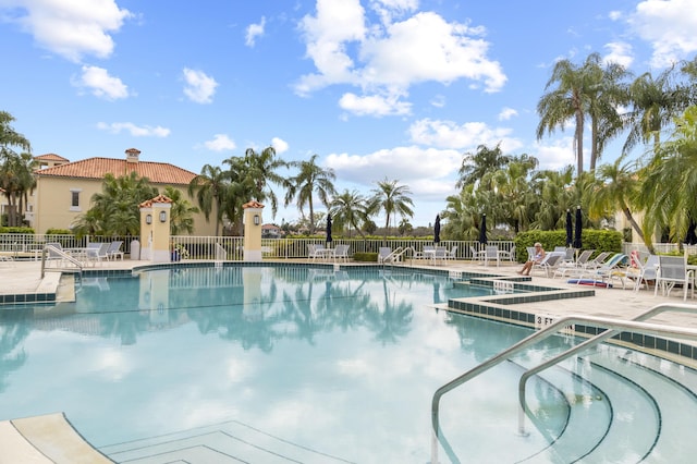 community pool with a patio area, fence, and a hot tub