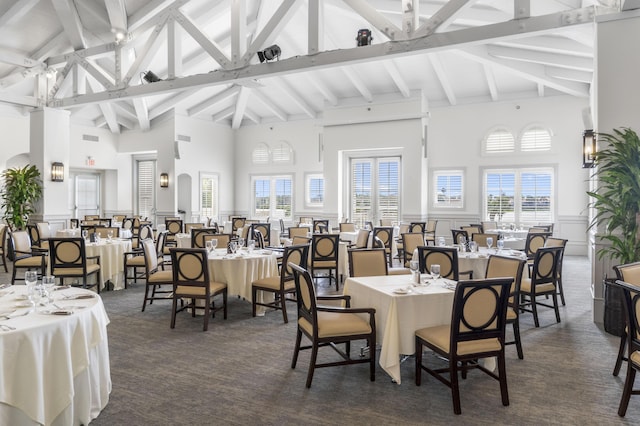 dining area featuring high vaulted ceiling, a decorative wall, a wainscoted wall, beamed ceiling, and dark carpet