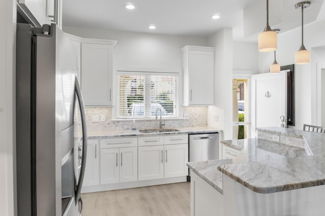 kitchen with stainless steel appliances, backsplash, white cabinets, a sink, and light wood-type flooring