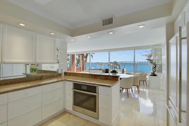 kitchen with visible vents, white cabinets, ornamental molding, a peninsula, and stainless steel oven