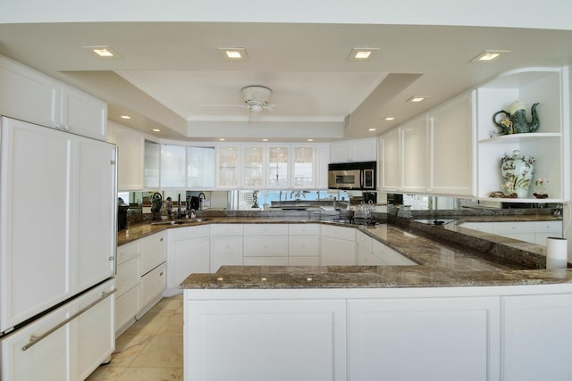 kitchen with paneled built in fridge, white cabinets, stainless steel microwave, a tray ceiling, and open shelves