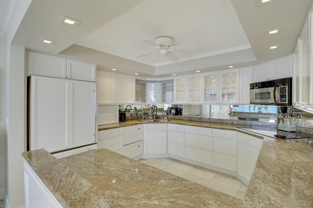 kitchen with a raised ceiling, light stone counters, stainless steel microwave, paneled fridge, and a sink