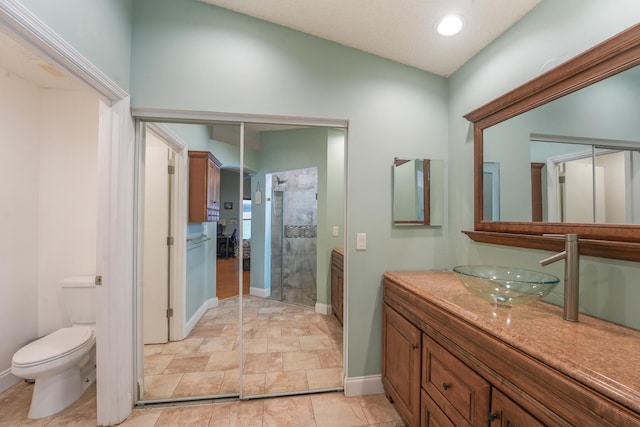 bathroom featuring recessed lighting, toilet, vanity, tiled shower, and baseboards