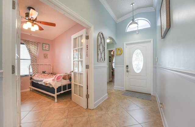 foyer entrance featuring light tile patterned floors, arched walkways, a textured ceiling, lofted ceiling, and crown molding