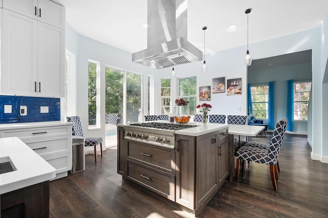 kitchen with light countertops, stainless steel gas stovetop, backsplash, white cabinets, and wall chimney range hood