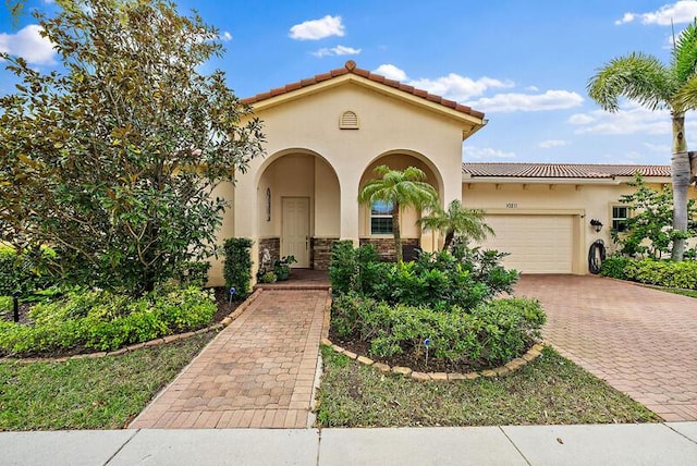 mediterranean / spanish home featuring a garage, stone siding, a tile roof, decorative driveway, and stucco siding