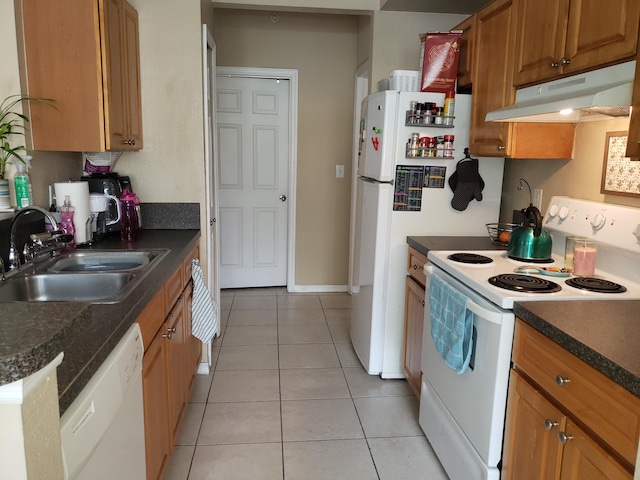 kitchen with white appliances, light tile patterned floors, dark countertops, under cabinet range hood, and a sink