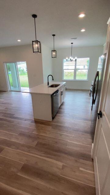 kitchen featuring light wood finished floors, appliances with stainless steel finishes, hanging light fixtures, light countertops, and a sink