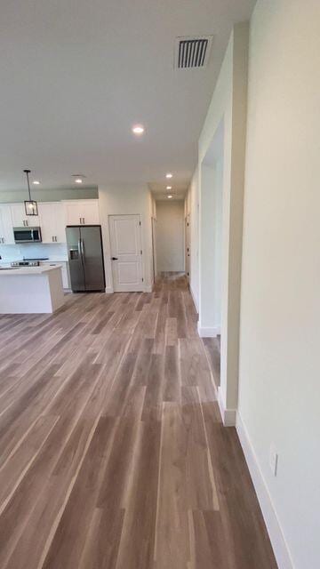 interior space with wood finished floors, visible vents, refrigerator with ice dispenser, white cabinets, and stainless steel microwave