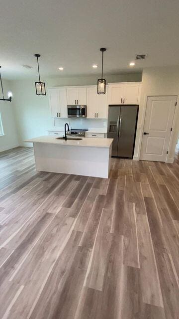 kitchen featuring black refrigerator with ice dispenser, stainless steel microwave, a sink, and white cabinetry