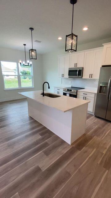 kitchen featuring an island with sink, appliances with stainless steel finishes, light countertops, white cabinetry, and a sink