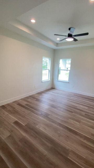 spare room with a tray ceiling, baseboards, and wood finished floors