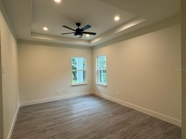 unfurnished room with baseboards, a tray ceiling, and dark wood-style flooring