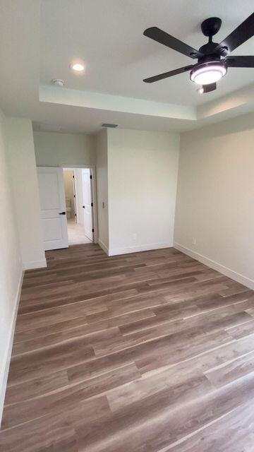 spare room with wood finished floors, recessed lighting, a raised ceiling, and baseboards