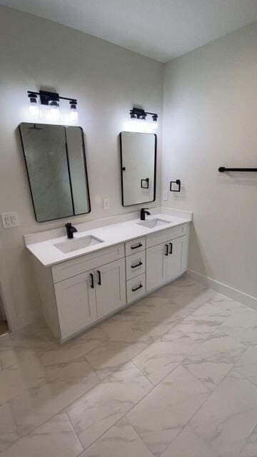 full bathroom with marble finish floor, a sink, baseboards, and double vanity