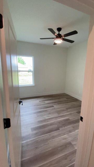 empty room with wood finished floors, a ceiling fan, and baseboards