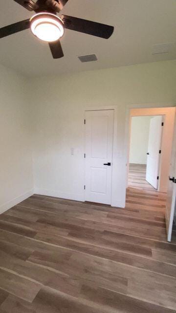 empty room with visible vents, wood finished floors, a ceiling fan, and baseboards