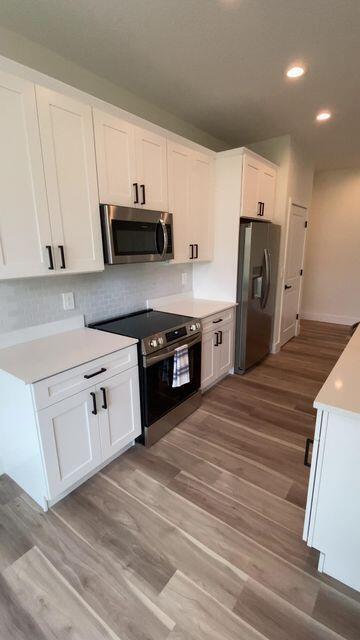 kitchen featuring stainless steel appliances, light countertops, light wood-type flooring, white cabinetry, and recessed lighting